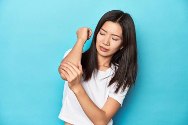 Beyaz tişörtlü genç Asyalı kadın, stüdyo fotoğrafı, dirsek masajı, kötü bir hareketin ardından acı çeken..