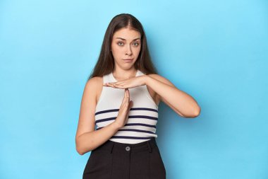 Çizgili bluzlu bir kadın mavi bir stüdyoda poz veriyor..