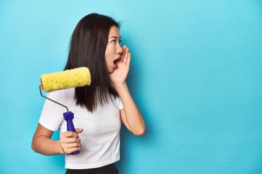 Boyalı silindirli genç Asyalı kadın, DIY konsepti, bağırıyor ve avuç içini açık tutuyor..