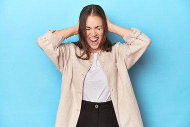 Mavi arka planda, mavi gömlekli şık genç bir kadın. Kulakları kulaklarıyla kapatıyor. Çok fazla ses duymamaya çalışıyor..