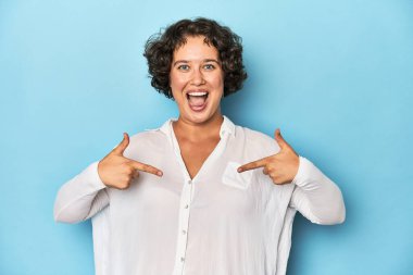 Kısa saçlı, genç, beyaz bir kadın parmaklarıyla işaret ederek şaşırdı, geniş bir gülümsemeyle..