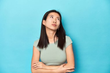 Yazın yeşil bluzlu Asyalı kadın, stüdyo arkaplanı, tekrarlanan bir görevden bıkmış..