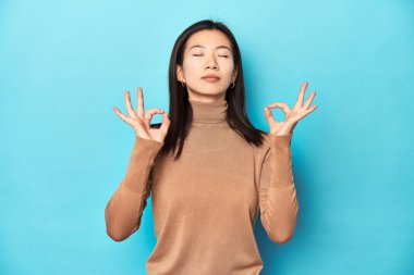 Kahverengi balıkçı yakalı genç Asyalı kadın yoğun bir günün ardından rahatlıyor. Yoga yapıyor..