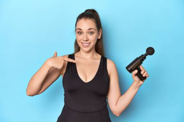 Mavi bir stüdyoda elektrikli masaj aleti olan aktif bir kadın gömlek fotokopi odasını elle gösteriyor, gururlu ve kendinden emin.