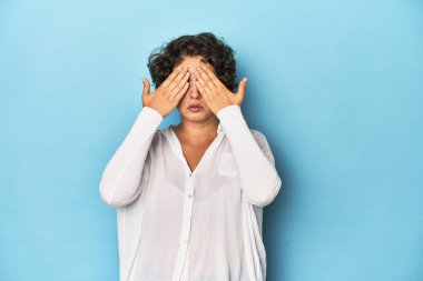 Kısa saçlı, genç, beyaz bir kadın elleriyle gözlerini kapatmaktan korkuyor..