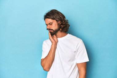 Beyaz gömlekli sakallı adam, mavi arka planda güçlü bir diş ağrısı, azıdişi ağrısı var..