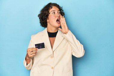 Kredi kartıyla genç bir kadın, zarif beyaz bir ceket bağırıyor ve avuç içi açık bir şekilde ağzını tutuyor..