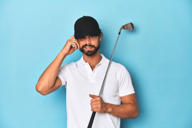 Uzun saçlı golf sopası ve kulakları kulaklarla kaplı bir şapkası var..
