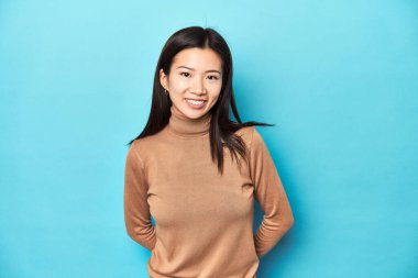 Kahverengi balıkçı yakalı genç Asyalı kadın, mutlu, gülümseyen ve neşeli..