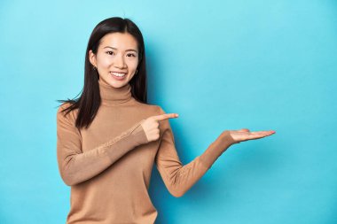 Kahverengi balıkçı yakalı genç Asyalı kadın, palmiye ağacında bir fotokopi yeri tutarken heyecanlanıyor..