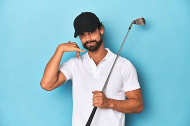 Golf sopası ve şapkası olan uzun saçlı bir golfçü cep telefonu hareketini parmaklarıyla gösteriyor..