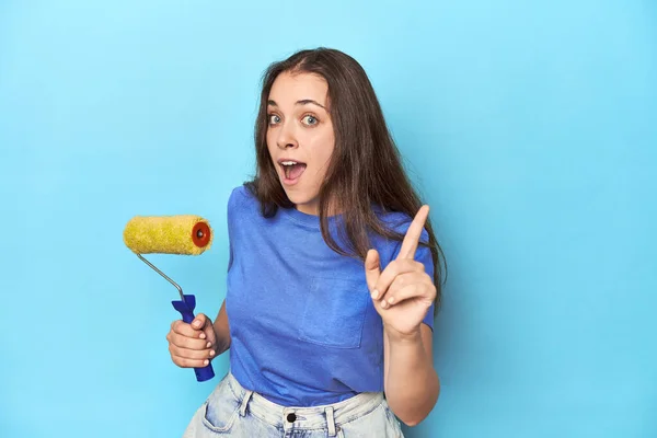 アイデア インスピレーションのコンセプトを持つ青い背景に黄色いペイントローラーを持つ若い女性 — ストック写真