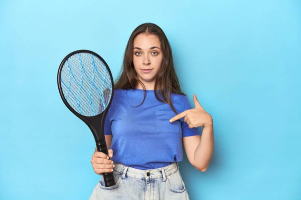 シャツのコピースペースを手で指す青い背景の人に電気バグバッパーを持つ女性 誇りと自信 — ストック写真