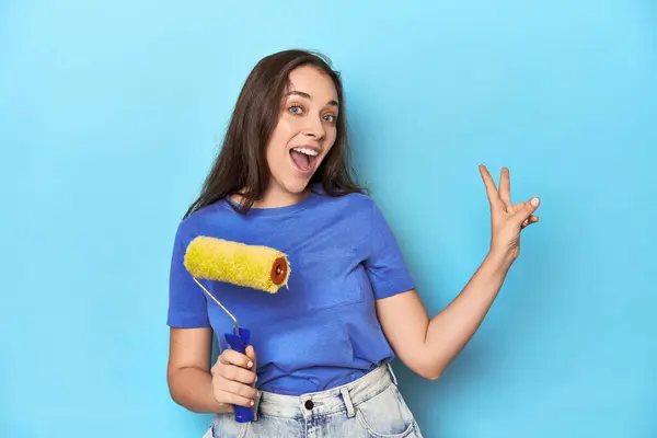 Jonge Vrouw Met Gele Verfrol Een Blauwe Achtergrond Vrolijk Zorgeloos — Stockfoto