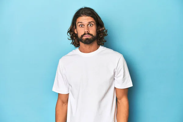 Bearded Man White Shirt Blue Backdrop Shrugs Shoulders Open Eyes — Stock Photo, Image