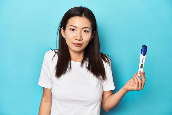 Young Asian woman holding a pregnancy test, studio shot.