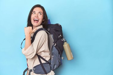 Mavi noktalarda sırt çantalı maceraperest bir kadın başparmağı uzakta, gülüyor ve kaygısız..