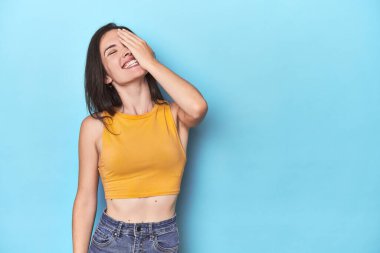 Mavi arka planda gülen, gülen, kaygısız, doğal duyguları olan beyaz bir kadın..