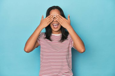 Mavi stüdyodaki Filipinli genç kadın elleriyle gözlerini kapatıyor, büyük bir gülümsemeyle bir sürpriz bekliyor..