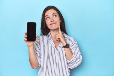 Mavi arkaplanda telefon ekranı gösteren kadın