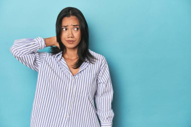 Mavi stüdyodaki Filipinli genç kadın kafasının arkasına dokunuyor, düşünüyor ve bir seçim yapıyor..