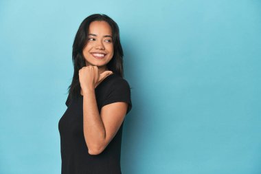 Mavi stüdyodaki Filipinli genç kadın başparmağı uzakta, gülüyor ve kaygısız.