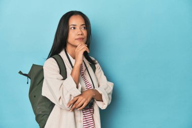 Kameralı ve sırt çantalı Filipinli kadın şüpheli ve şüpheci bir ifadeyle yana bakıyor..