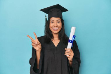 Mavi stüdyodaki diplomasıyla Filipinli. İki numarayı parmaklarıyla gösteriyor..