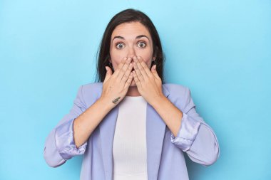 Mavi arka plandaki mavi ceketli kadın şok oldu. Ağzını ellerle kapladı. Yeni bir şey keşfetmeye can atıyor..