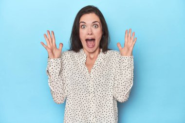 Mavi arka planda zaferi ya da başarıyı kutlayan genç beyaz kadın şaşırdı ve şok oldu..