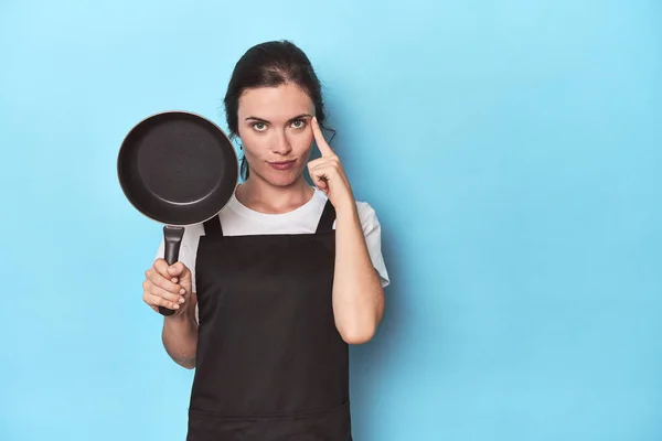 Woman Apron Pan Blue Background Pointing Temple Finger Thinking Focused — Stock Photo, Image