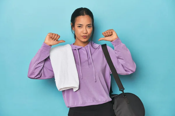 Filipina with gym gear on blue studio feels proud and self confident, example to follow.