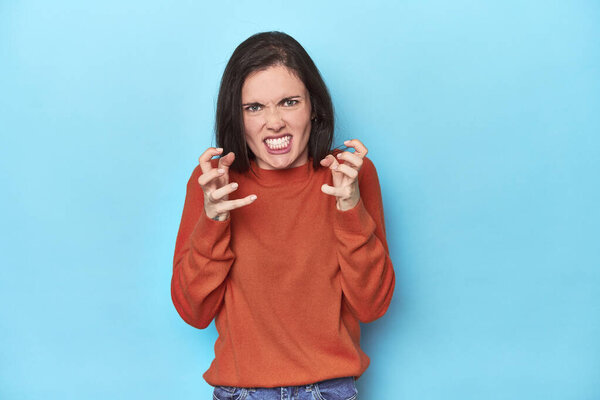 Молодая белая женщина на синем фоне расстроена криками напряженных рук.