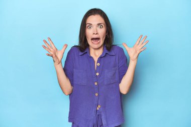 Mavi arka planda genç beyaz kadın gökyüzüne haykırıyor, yukarı bakıyor, hayal kırıklığına uğramış..