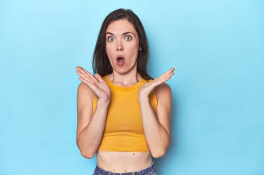 Mavi arka plandaki genç beyaz kadın şaşırdı ve şok oldu..