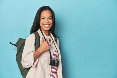 Filipinli kadın kamera ve sırt çantasıyla Blues yapıyor ve başparmağını kaldırıyor.