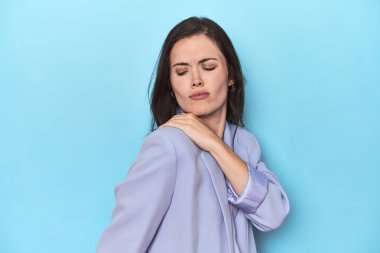 Mavi ceketli, mavi arka planda omuz ağrısı olan bir kadın..