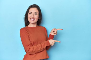 Mavi arka plandaki genç beyaz kadın işaret parmağıyla işaret ettiği için heyecanlı..