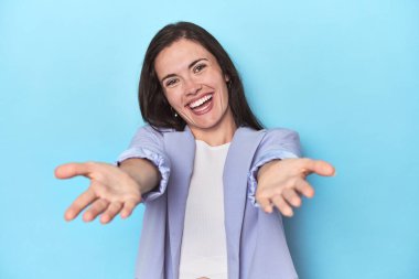 Mavi arka plandaki mavi ceketli kadın kameraya sarıldığı için kendinden emin..