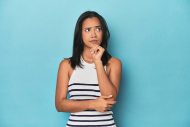 Filipinli genç kadın mavi stüdyoda düşünüyor, bakıyor, yansıtıyor, düşünüyor, hayal kuruyor..