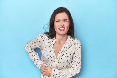 Mavi arka planda karaciğer ağrısı çeken, karnı ağrıyan beyaz bir kadın..