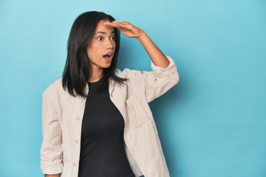 Mavi stüdyodaki Filipinli genç kadın çok uzaklara bakıyor ve elini alnına koyuyor..