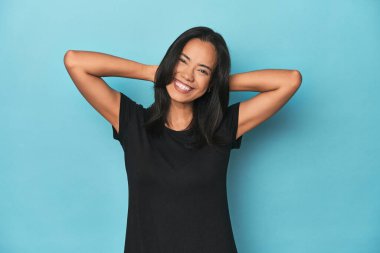 Mavi stüdyodaki Filipinli genç kadın kollarını açıyor, rahat pozisyonda..