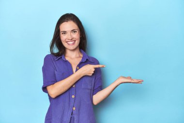 Mavi arka plandaki genç beyaz kadın, elinde bir fotokopi odası tutarken heyecanlanıyor..