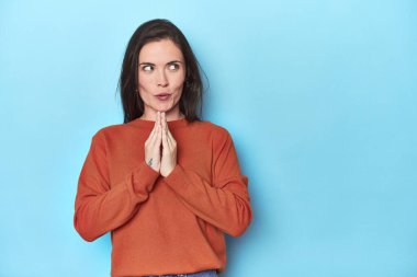 Kafkasyalı genç bir kadın mavi arka planda bir plan yapıyor, bir fikir kuruyor..