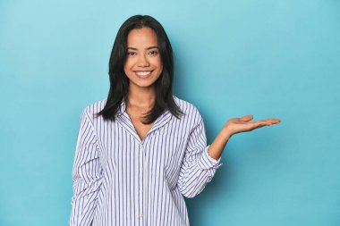 Mavi stüdyodaki Filipinli genç kadın bir avuç içinde fotokopi alanı gösteriyor ve belinde bir el daha tutuyor..