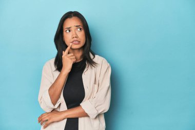 Mavi stüdyodaki Filipinli genç kadın şüpheli ve şüpheci bir ifadeyle yana bakıyor..