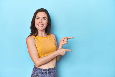 Mavi arka plandaki genç beyaz kadın işaret parmağıyla işaret ettiği için heyecanlı..