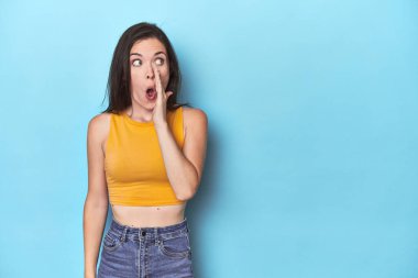 Mavi arka plandaki genç beyaz kadın gizli bir sıcak fren haberi veriyor ve yana bakıyor.