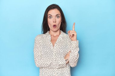 Mavi arka planda oturan beyaz bir kadının harika bir fikri var, yaratıcılık kavramı..